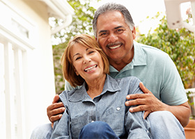 A man and woman smiling sitting on a porch after receiving dental implants