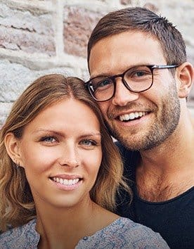 Man and woman smiling with brick wall in background