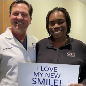 Doctor Michael Kirk and patient smiling together, holding a sign that promotes dental health and smiles.
