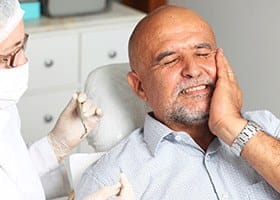 Man in dental chair holding cheek in pain