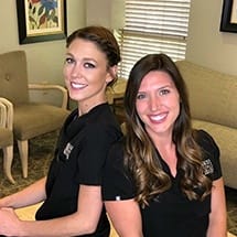 Two smiling dental team members standing back to back