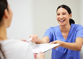 Smiling team member giving patient dental insurance form