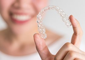 Smiling person holding an Invisalign clear aligner in Oklahoma City
