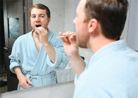 young man in robe brushing teeth 