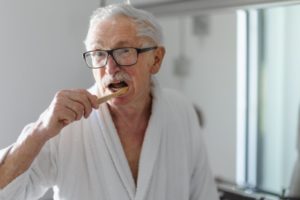 older man in robe brushing teeth