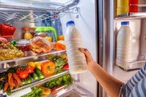 man holding milk in front of fridge filled with vegetables 